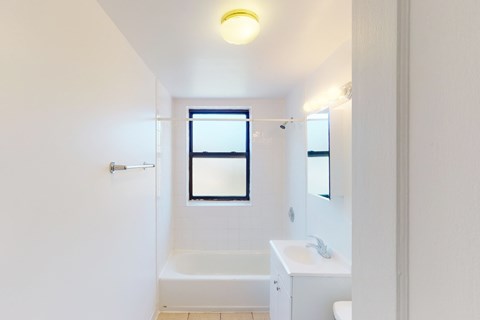 A white bathroom with a window and a bathtub.