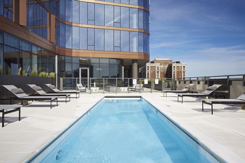 A swimming pool on a rooftop with lounge chairs around it.