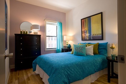 A bedroom with a blue bedspread and a painting on the wall.