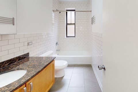 A white tiled bathroom with a brown granite counter top.