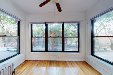 A room with a ceiling fan and large windows.