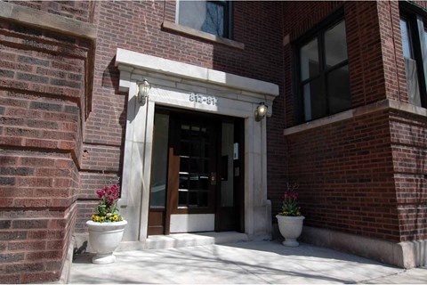 The front door of a brick building with a white trim and two planters with flowers on either side.