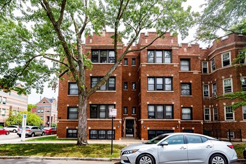A silver car is parked in front of a brick building.