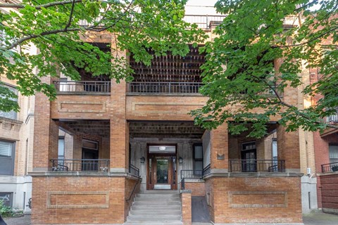 A building with a balcony and a doorway is surrounded by trees.