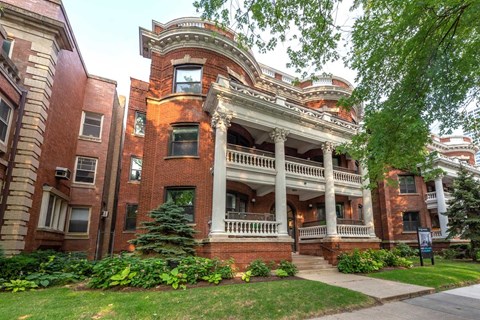 A large red brick building with a balcony and a tree in front.