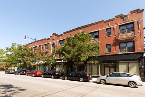 A row of parked cars on a street in front of a red brick building.