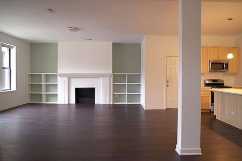 A large empty room with a fireplace and wooden floors.