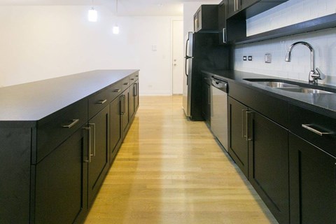 A kitchen with black cabinets and a wooden floor.