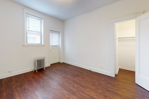 A room with a wooden floor and a white wall with a window and a radiator.