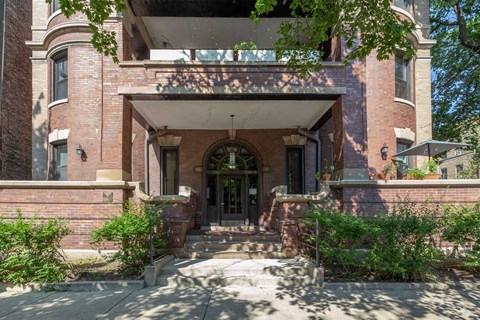 A large, old building with a front porch and a staircase leading to the entrance.
