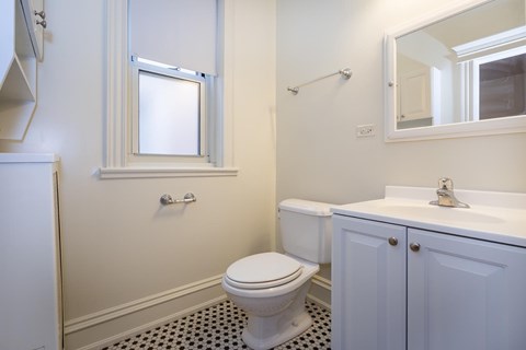A white toilet with a window above it in a bathroom.