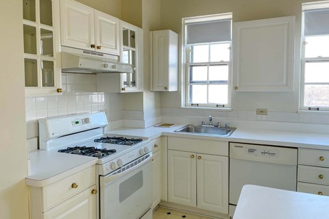 A white kitchen with a stove, sink, and cabinets.