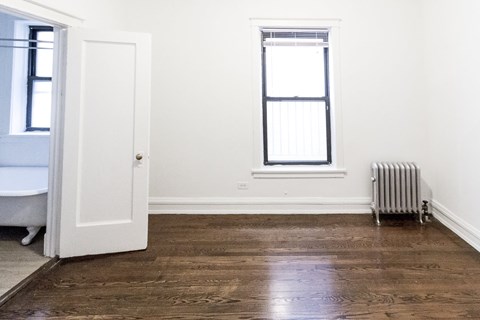 A room with a white door, a window with blinds, and a radiator on the wall.