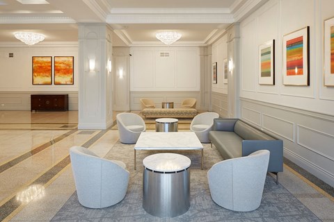 A spacious lobby with a white marble floor and grey chairs.
