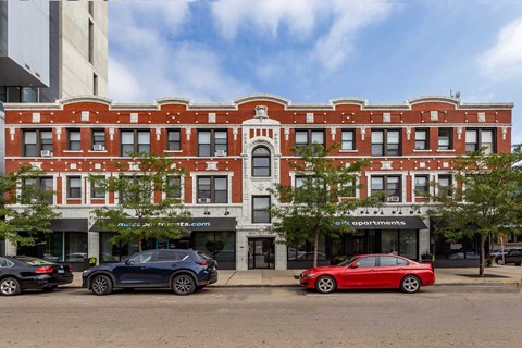 Two cars parked in front of a red building with a sign that says apartments.