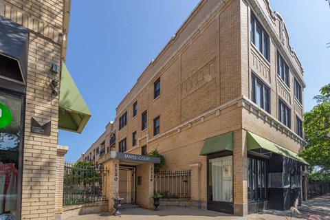A brick building with a green awning and a sign that says Maple Court.