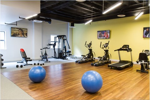 A gym with a variety of equipment including treadmills, stationary bikes, and exercise balls.
