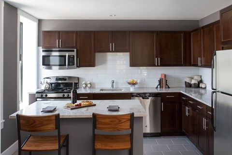 A kitchen with a white counter top and wooden chairs.