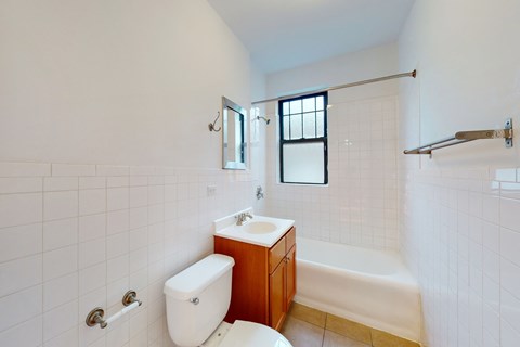 A white tiled bathroom with a toilet, sink, and bathtub.