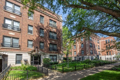A row of red brick apartment buildings with green trees in front.