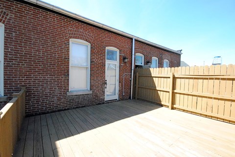 A wooden deck in front of a brick building with a white door.