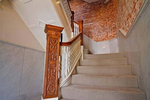 A staircase with a wooden handrail and a brick wall in the background.