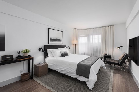 A modern bedroom with a large bed, a chair, and a painting on the wall.
