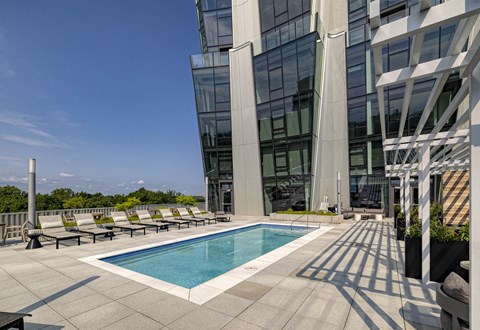 A swimming pool on a rooftop patio with lounge chairs and a modern building in the background.