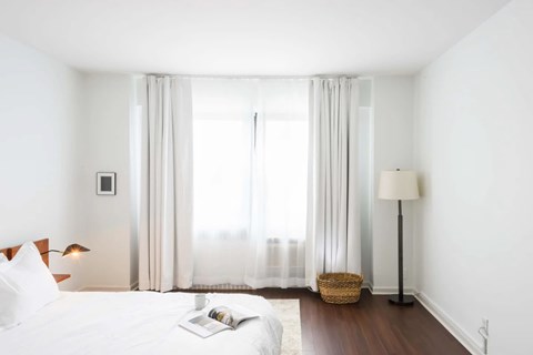 A white bedroom with a large bed and a window with curtains.