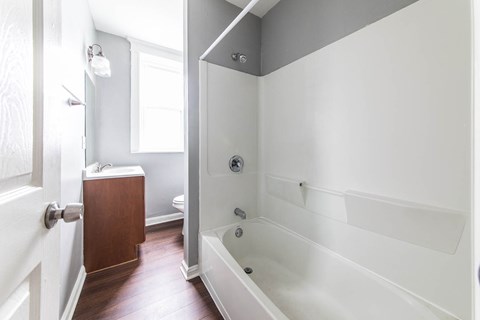 A white bathroom with a wooden cabinet and a white bathtub.