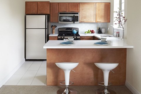 A kitchen with a refrigerator, microwave, oven, and a counter with two white pedestal tables.