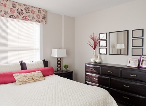 A bedroom with a white bed, a red pillow, and a white lamp.