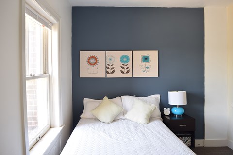 A bedroom with a bed, pillows, a lamp, and pictures on the wall.
