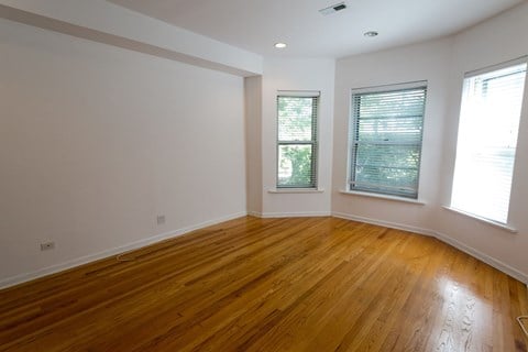 A room with wooden flooring and two windows.