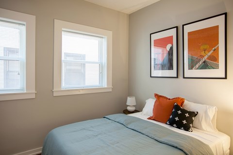 A bedroom with a bed, two pillows, and two framed pictures on the wall.