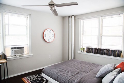A bedroom with a bed, a ceiling fan, and a clock on the wall.