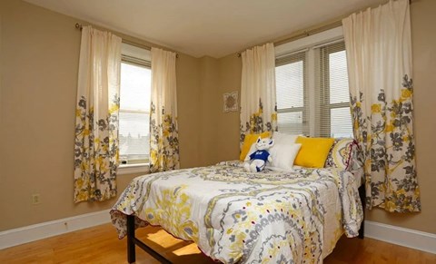 A bedroom with a bed in the center and floral curtains on the windows.