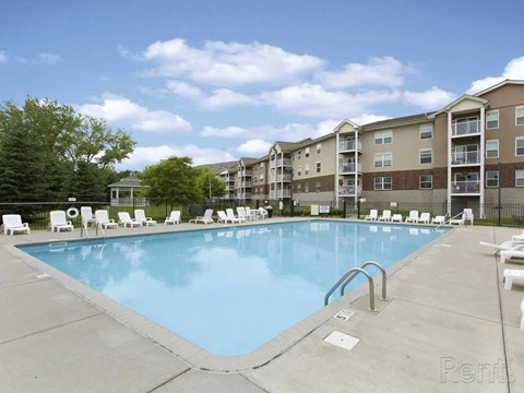 A large swimming pool surrounded by lounge chairs and apartment buildings.
