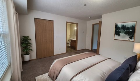 A bedroom with a bed, a plant, and a painting on the wall.