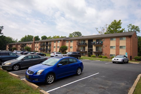 A blue car is parked in a parking lot in front of a brick apartment building.