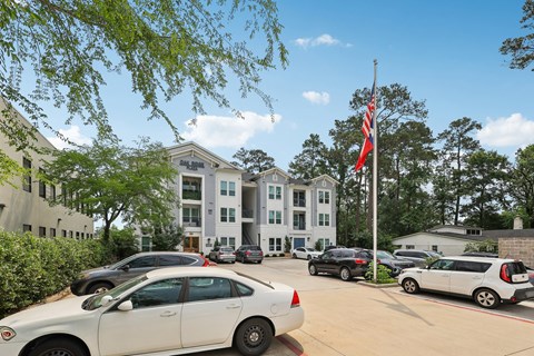 A white car is parked in front of a building with a flag on a pole.