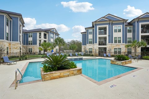 A swimming pool surrounded by a stone wall and chairs in front of apartment buildings.