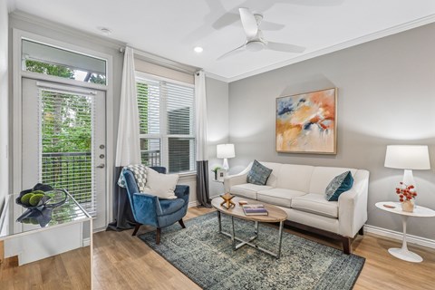 A living room with a blue chair, a white couch, and a painting on the wall.