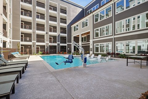 A large outdoor pool area with sun loungers and a building in the background.