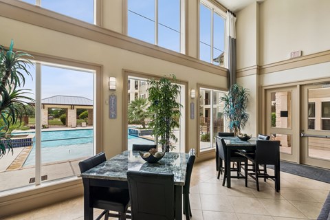 A dining room with a table and chairs and a pool outside the window.