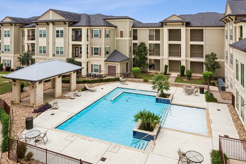 A large swimming pool is surrounded by a patio with chairs and a table.