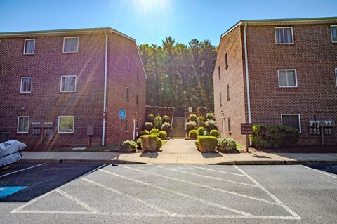 A sunny day at a brick apartment complex with a parking lot in the foreground.