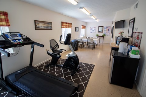 A room with a treadmill, exercise bike, and a table with chairs.