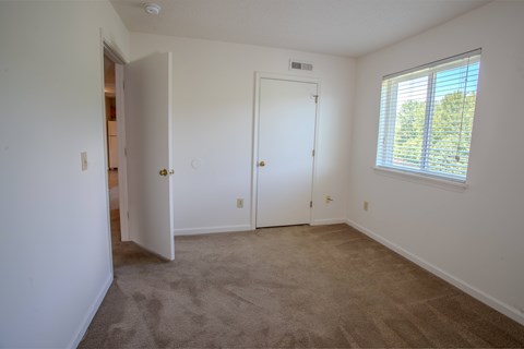 A room with a carpeted floor, a white door, and a window with blinds.