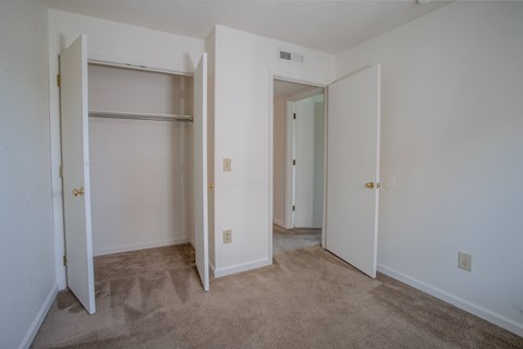 A room with white walls and carpeted floor with two open doors.